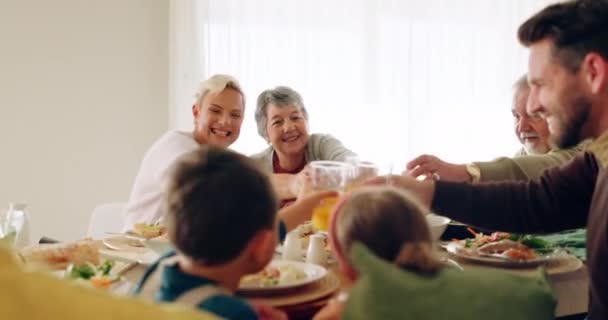 Family, lunch and juice toast in dining room with love, bonding and conversation at home. Food, cheers and children with grandparents, parents and orange fruit drink for brunch, meal or celebration. - Imágenes, Vídeo
