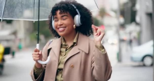 Mujer feliz, auriculares y escuchar música en la ciudad con paraguas para la transmisión de audio al aire libre. Emocionada mujer caminando bajo la lluvia con auriculares para banda sonora y bailando en una ciudad urbana. - Metraje, vídeo