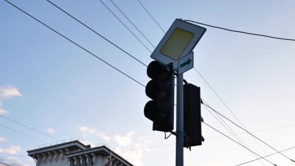 Дорожный вертикальный европейский светофор на главной дороге со знаком в городе на фоне неба, красного, янтарного, зеленого цветов. Средний выстрел. Статический - Кадры, видео