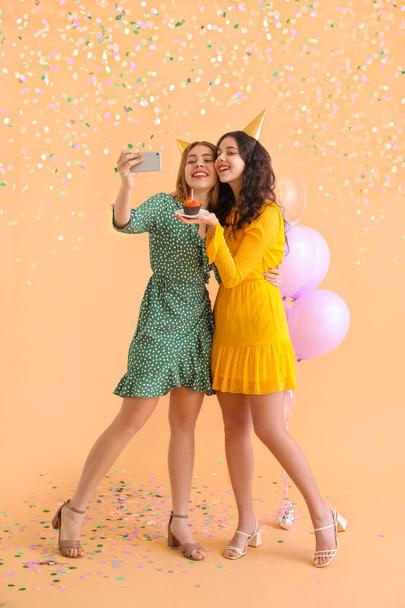 Mutlu genç kadınlar ve doğum günü keki bej arka planda selfie çekiyorlar. - Fotoğraf, Görsel