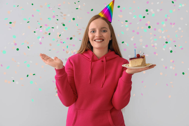 Красивая женщина с кусочком торта празднует день рождения на сером фоне - Фото, изображение