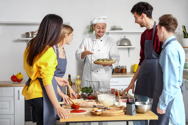 Chef italiano com pizza preparada e grupo de jovens após aula de culinária na cozinha - Foto, Imagem