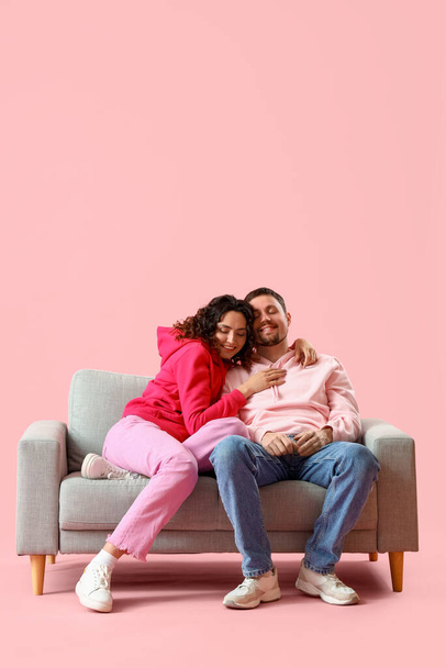 Fiatal pár ül kanapén szemben rózsaszín háttér - Fotó, kép