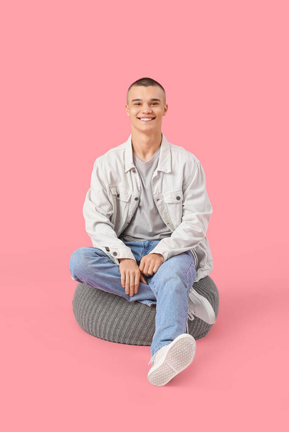 Feliz joven sentado en otomana sobre fondo rosa - Foto, imagen