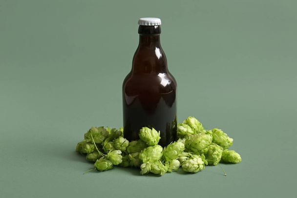 Свежий зеленый хмель и бутылка холодного пива на цветном фоне - Фото, изображение