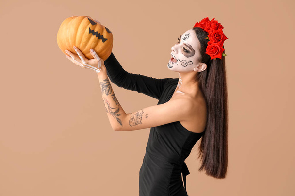 Hermosa mujer joven vestida como novia muerta para la fiesta de Halloween con calabaza sobre fondo beige - Foto, imagen