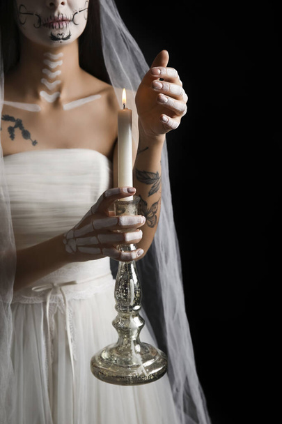 Jonge vrouw verkleed als dode bruid voor Halloween feest met kandelaar met kaars op zwarte achtergrond - Foto, afbeelding