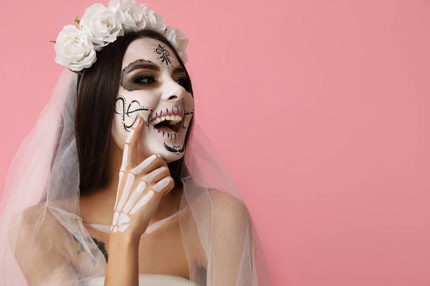 Mooie jonge vrouw verkleed als dode bruid voor Halloween feest op roze achtergrond - Foto, afbeelding