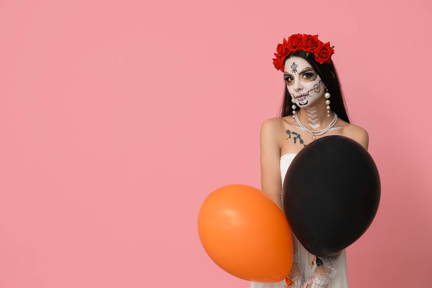 Hermosa joven vestida de novia muerta para la fiesta de Halloween con globos sobre fondo rosa - Foto, imagen