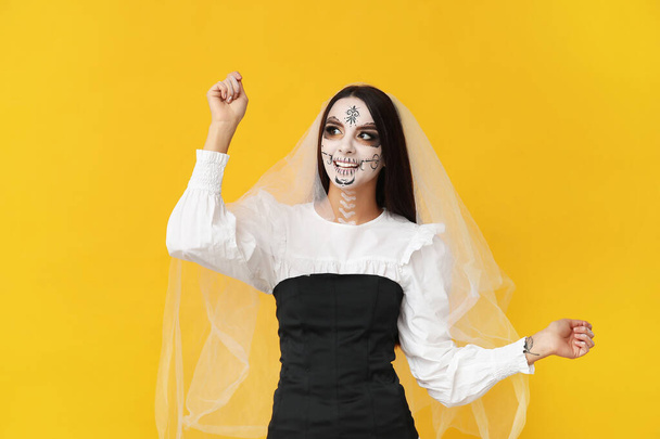 Mooie jonge vrouw verkleed als dode bruid voor Halloween feest op gele achtergrond - Foto, afbeelding