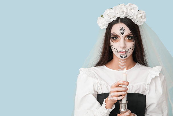 Jonge vrouw verkleed als dode bruid voor Halloween feest met kandelaar met kaars op blauwe achtergrond - Foto, afbeelding