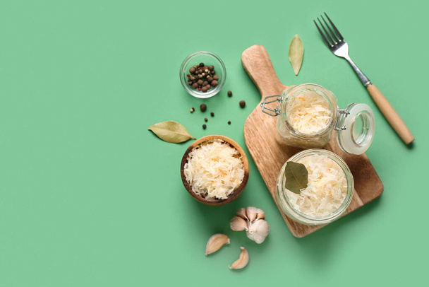 Gläser und Schale mit schmackhaftem Sauerkraut mit Zutaten auf grünem Hintergrund - Foto, Bild