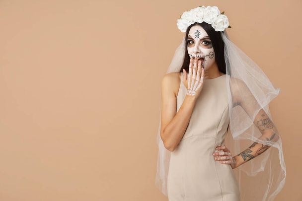 Hermosa mujer joven sorprendida vestida como novia muerta para la fiesta de Halloween sobre fondo beige - Foto, imagen