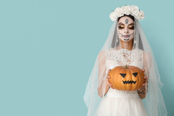 Красивая молодая женщина, одетая как мертвая невеста на вечеринке Хэллоуина с тыквой на синем фоне - Фото, изображение