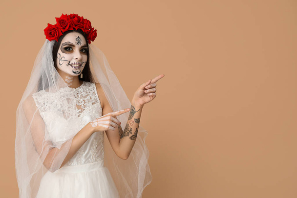 Kaunis nuori nainen pukeutunut kuollut morsian Halloween osapuoli osoittaa jotain beige tausta - Valokuva, kuva