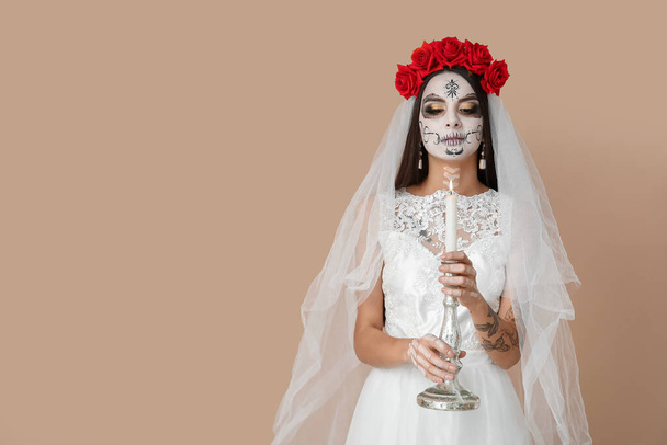 Jeune femme habillée en mariée morte pour Halloween fête tenant chandelier avec bougie sur fond beige - Photo, image