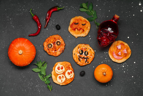 Samenstelling met verschillende smakelijke Halloween mini pizza 's en fles drank op donkere achtergrond - Foto, afbeelding