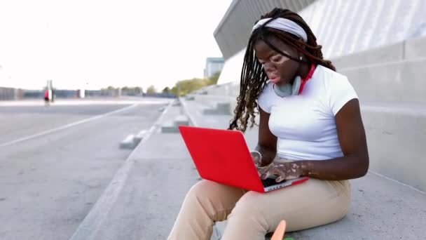 Joven estudiante africana con vitiligo utilizando el ordenador portátil sentado al aire libre. Mujer negra milenaria trabajando en la computadora. Concepto de juventud y tecnología. Copiar espacio para texto. - Imágenes, Vídeo