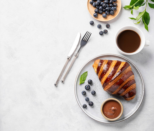 Friss croissant csokoládéval egy tányéron, világos háttérrel, áfonyával és egy csésze kávéval. Finom házi reggeli koncepció. Felülnézet és másolás.  - Fotó, kép