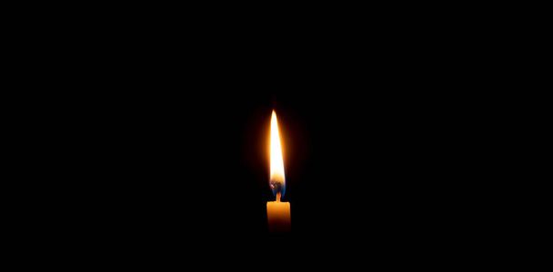 La llama o la luz de una sola vela ardiente brilla sobre una pequeña vela amarilla sobre fondo negro u oscuro en la mesa de la iglesia para Navidad, funeral o servicio conmemorativo con espacio para copias. - Foto, imagen