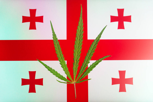 ジョージア国旗の背景にあるヘンプの葉です。 ジョージアのマリファナの栽培と使用に関する法律の合法化と変更の概念. - 写真・画像