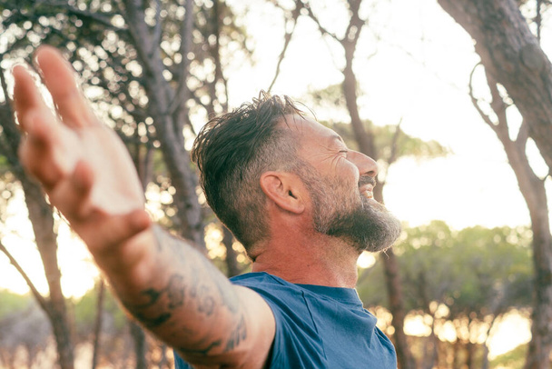 Closeup of side portrait man outstretching arms happy smiling and enjoying sunset light in outdoor nature leisure activity alone. Overjoyed serene expression adult mature male people outside enjoying - Photo, Image