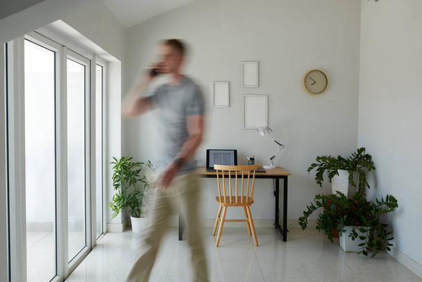 Movimiento borroso del hombre hablando por teléfono al caminar en su oficina en casa - Foto, Imagen