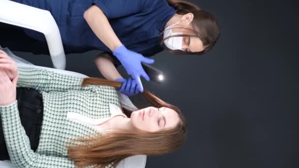 Az orvos trichológus megvizsgálja a női páciensek szőrszálait trichoscope-pal a klinikán. A trikhoscopos haj eljárása. Függőleges videó. - Felvétel, videó