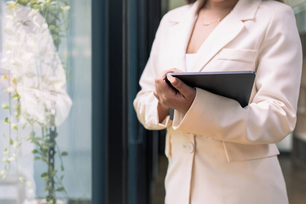 Femme d'affaires en costume tendance tenant tablette numérique debout près de la fenêtre du bureau. - Photo, image