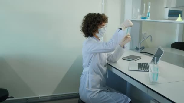 Panning left medium shot of female scientist sitting at desk looking at test tube, middle aged male coworker looking in microscope and young female lab assistant working with computer - Footage, Video