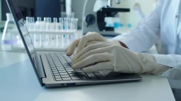 Focus op handen van onherkenbare medisch medewerker die overdag iets typt op toetsenbord in het laboratorium - Video