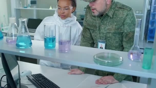 Tilt τόξο πυροβόλησε του στρατιωτικού άνδρα και της γυναίκας επιστήμονα στέκεται στο εργαστήριο κοιτάζοντας τις εικόνες των κυττάρων και των μορίων στην οθόνη του υπολογιστή - Πλάνα, βίντεο