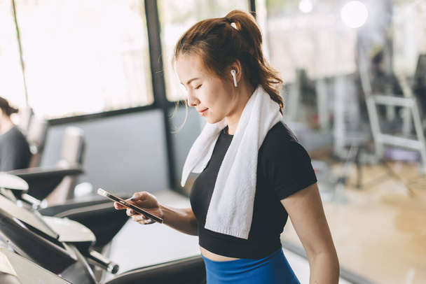 Sport woman on a treadmill using Smartphone checking Email reading news listening music or looking information from health tracking app. - Photo, Image