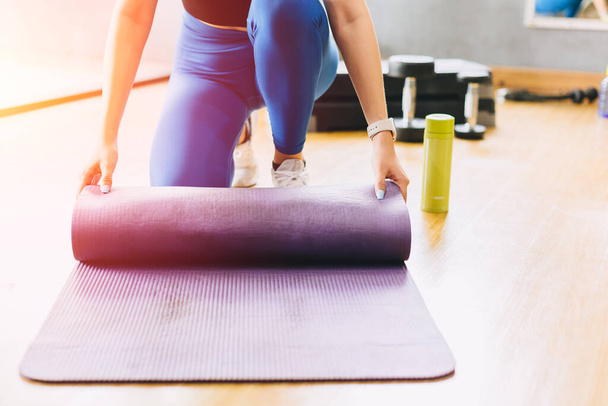 Closeup fitness woman in sport club studio with yoga mat. Young woman roll pilates mat at a fitness training class. - Photo, Image