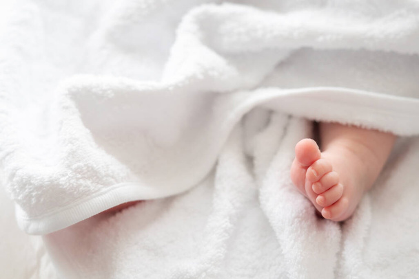 Sydäntä koskettava kuvaus puhtaasta viattomuudesta vastasyntyneenä babys jalka hellästi kurkistaa pehmeästä valkoisesta pyyhkeestä. - Valokuva, kuva