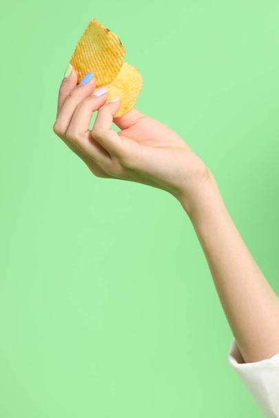 Азиатка держит картофельные чипсы в руке на зеленом фоне. - Фото, изображение
