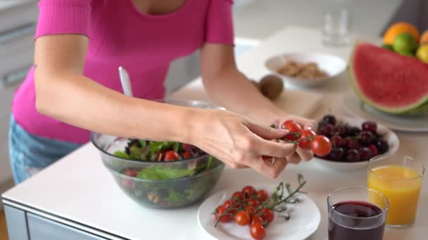 Lassú mozdulat egy felismerhetetlen lánytól, aki a konyhaasztalnál áll, és cseresznyés paradicsomot tölt egy tálba salátával és leveles zöldséggel.. - Felvétel, videó