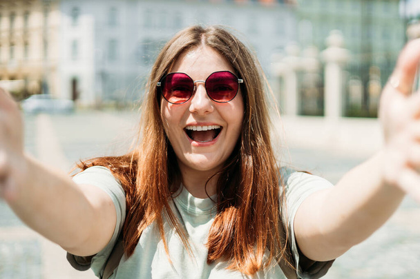 Foto relajada encantadora mujer joven positiva sostener la cámara y hacer selfie verano fuera en el centro de la ciudad al aire libre - Foto, imagen
