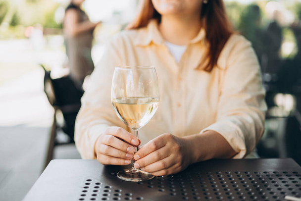 Weißweinglas in einem Café im Freien. Glückliche Frau, die auf der Caféterrasse an der Stadtstraße sitzt. Reisende. Frau stößt mit Wein an - Foto, Bild