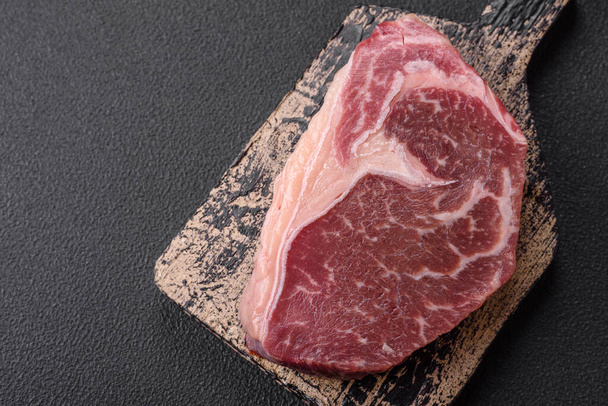 Friss nyers marhahús csíkos steak sóval, fűszerekkel és fűszernövényekkel sötét beton alapon - Fotó, kép