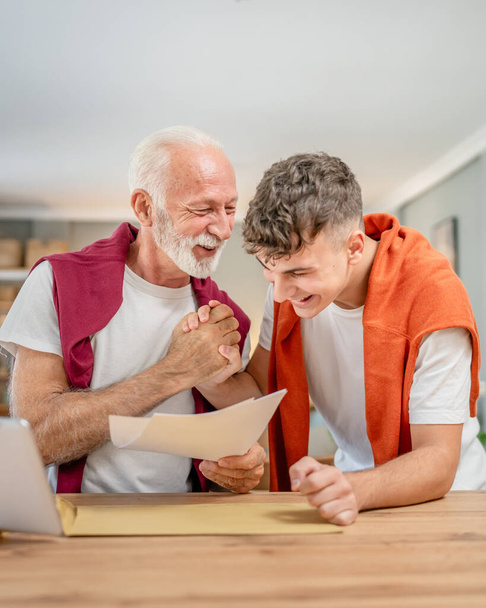 Senior man grandfather and caucasian man teenager boy grandson receive letter read good news student get scholarship or invitational letter from university share excitement real people - Photo, Image