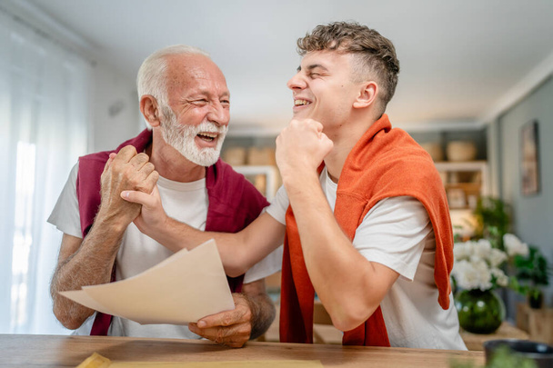 Senior man grandfather and caucasian man teenager boy grandson receive letter read good news student get scholarship or invitational letter from university share excitement real people - Photo, Image