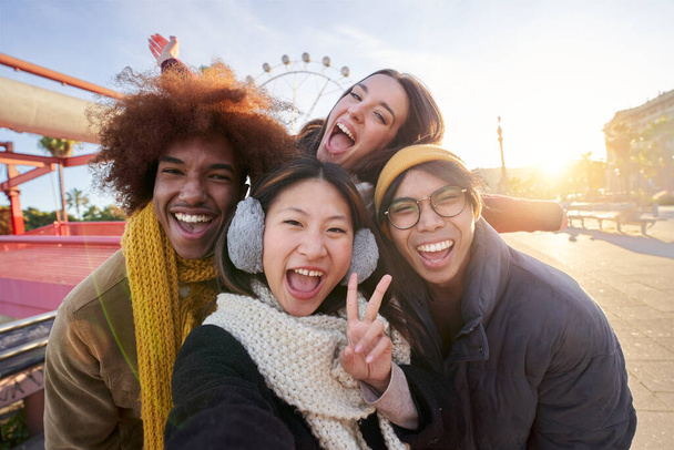 Groupe souriant excité d'amis multiraciaux prenant téléphone selfie drôle regardant la caméra debout ensemble en plein air. Jeunes multiethniques dans un parc d'attractions s'amusant pendant les vacances d'hiver ensoleillées.  - Photo, image