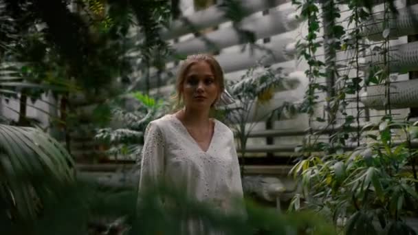 Спокойная мечтательная женщина в белом романтическом платье, пересекающая ботанический сад и касающаяся пальмового листа. Нежная молодая девушка отдыхает на тропических деревьях джунглей природы - Кадры, видео