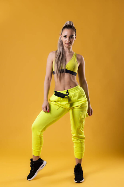 Beautiful girl in yellow outfit dancing zumba. Happy dance instructor against dark yellow or orange background. - 写真・画像
