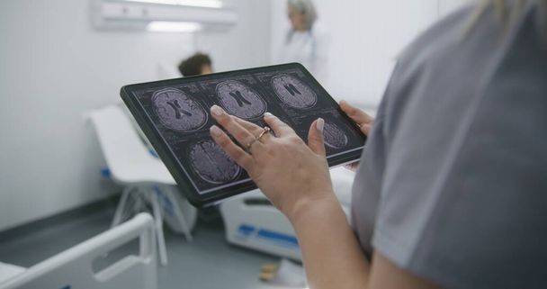 Зрілий лікар розмовляє з афроамериканським підлітком. Пацієнт лежить на ліжку в лікарні. Жінка-лікар вивчає результати МРТ або КТ-сканування на цифровому планшетному комп'ютері. Медичний персонал на роботі в сучасній клініці - Фото, зображення