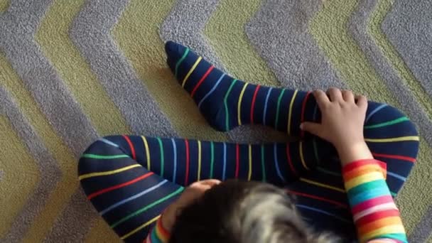 bovenaanzicht van kind met kleurrijke gestreepte sokken zittend op tapijt , - Video