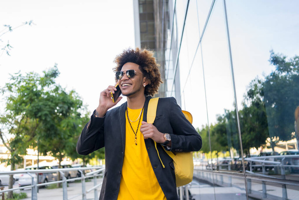 Casual stylish african american man talking to the phone while commuting with a bag - Fotografie, Obrázek