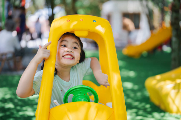 Linda niña asiática sonrisa juego juguete coche en la escuela o jardín de infantes patio o patio de recreo. Actividad saludable de verano para niños. Niño jugando en el patio al aire libre. Concepto de actividad infantil bebé. - Foto, imagen