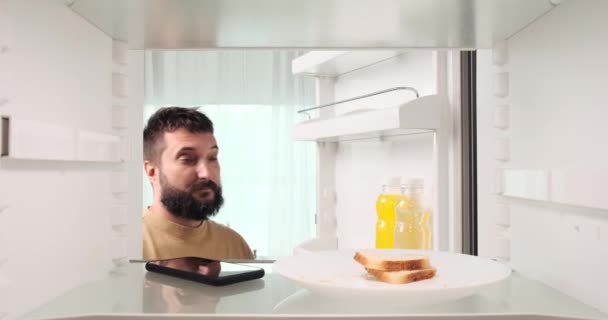 A bewildered Caucasian man, perhaps after a lively party, opens the fridge and is astonished to find his phone inside. His facial expression reflects the unexpected discovery. - Footage, Video